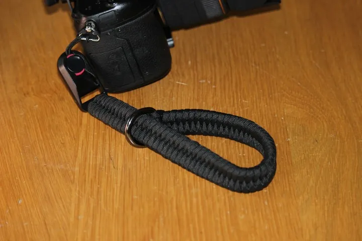 Black paracord camera wrist strap with quick-release buckle and steel D-ring fitted to a DSLR